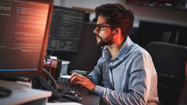 Man typing on computer in front of multiple screens